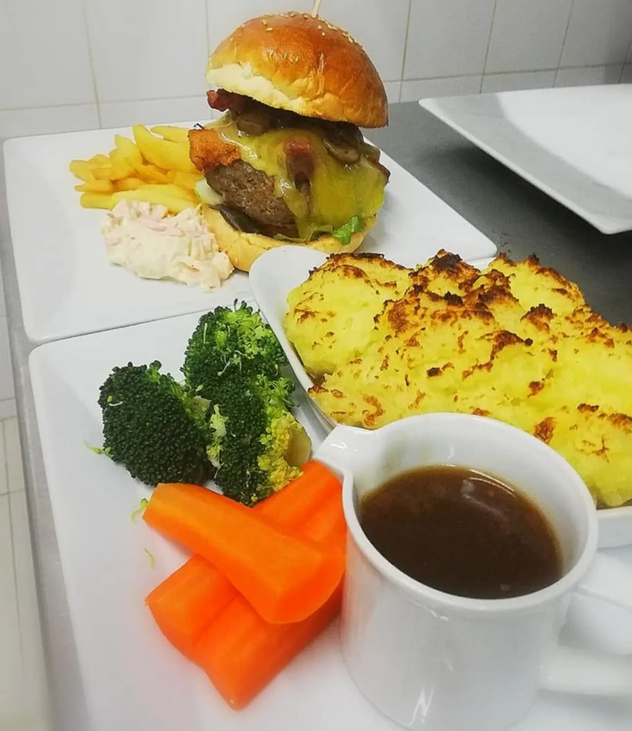 A burger with cheese and bacon, fries and coleslaw at the kitchen pass