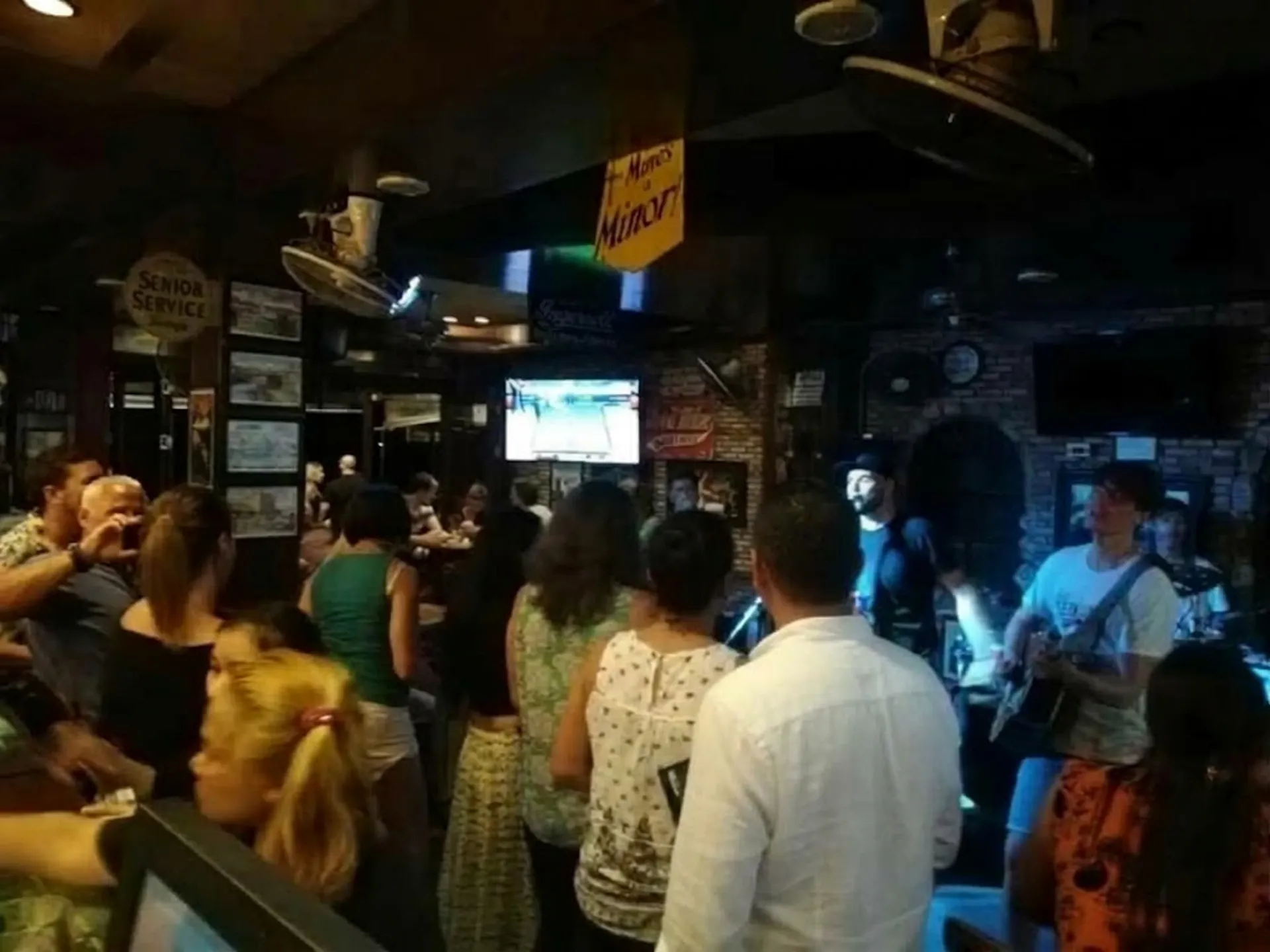 A live band with guitar, vocals and drums playing to a standing crowd inside the bar