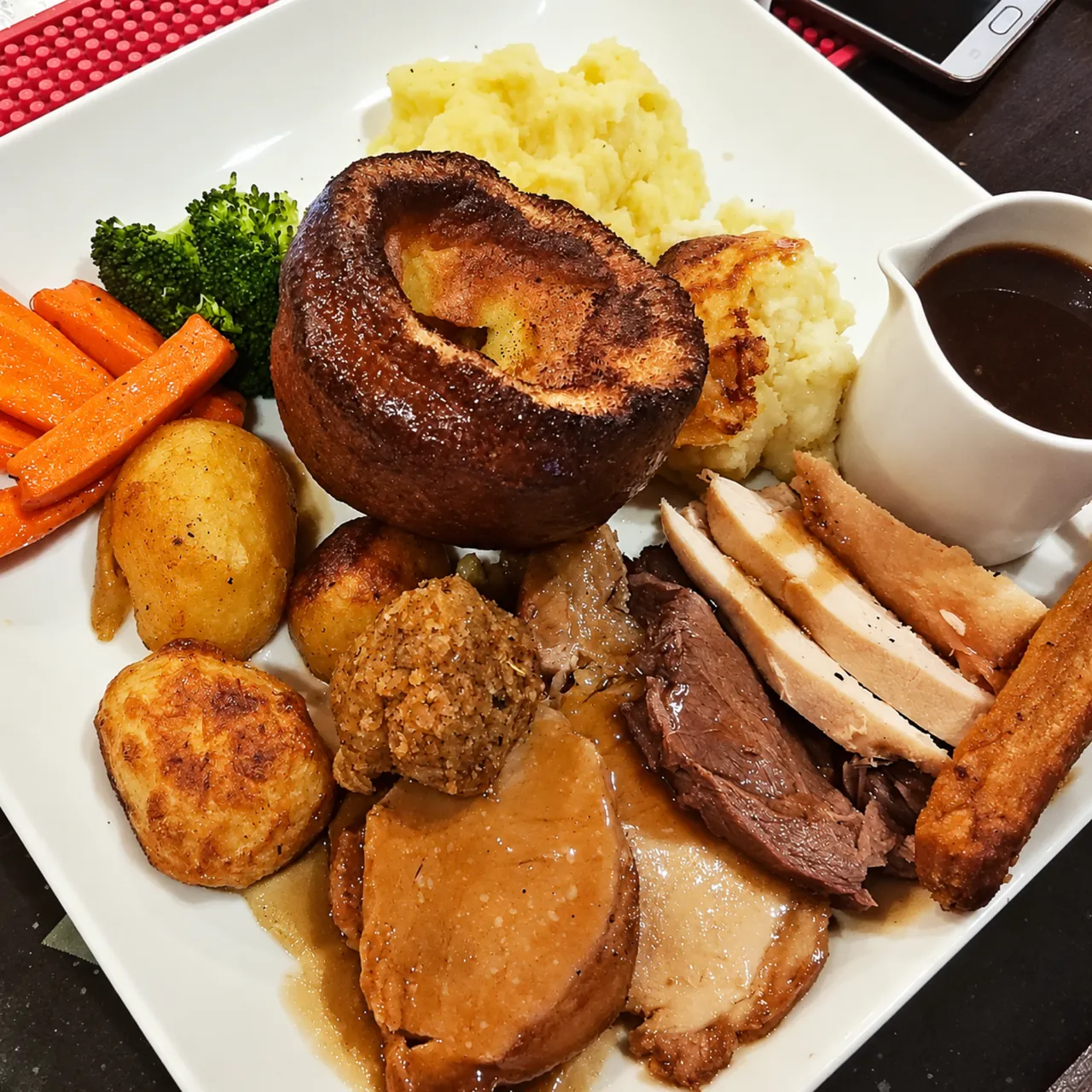 A Sunday roast from above: Yorkshire pudding, sliced roast meats, crackling, stuffing, roast and mashed potato, carrots, broccoli and a jug of gravy